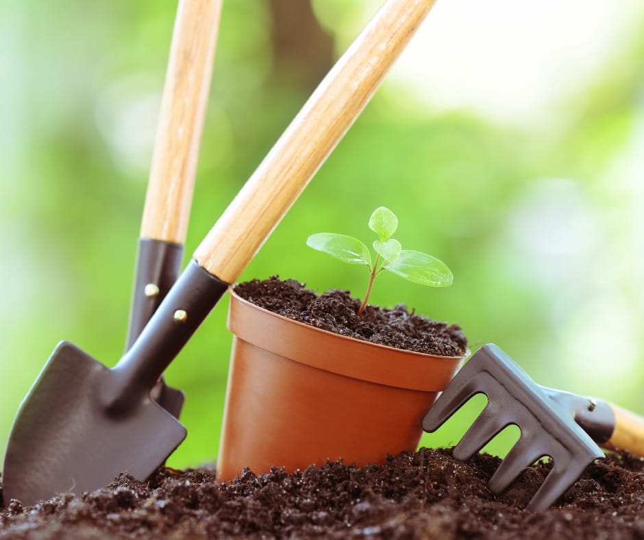 Puutarhatyökaluja ja ruukku mullan päälle aseteltuina